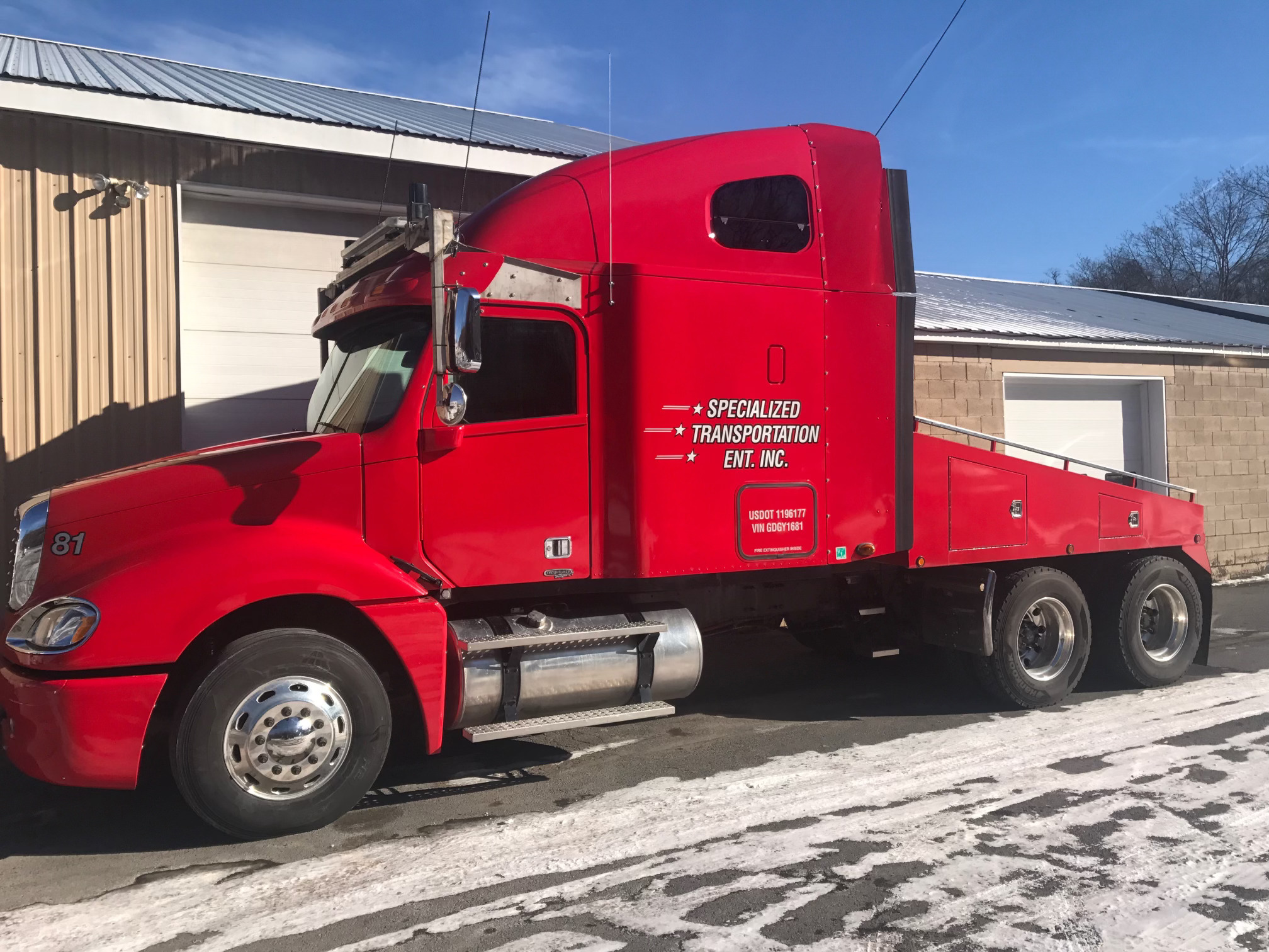 A red semi-truck parked beside a building on a snowy pavement.
