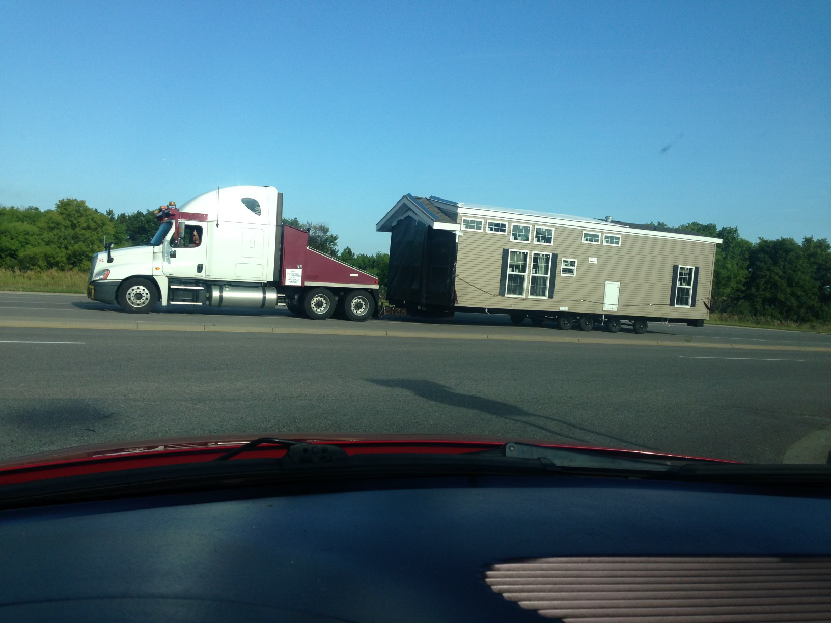 A semi-truck is towing a small house on a trailer along a roadway.